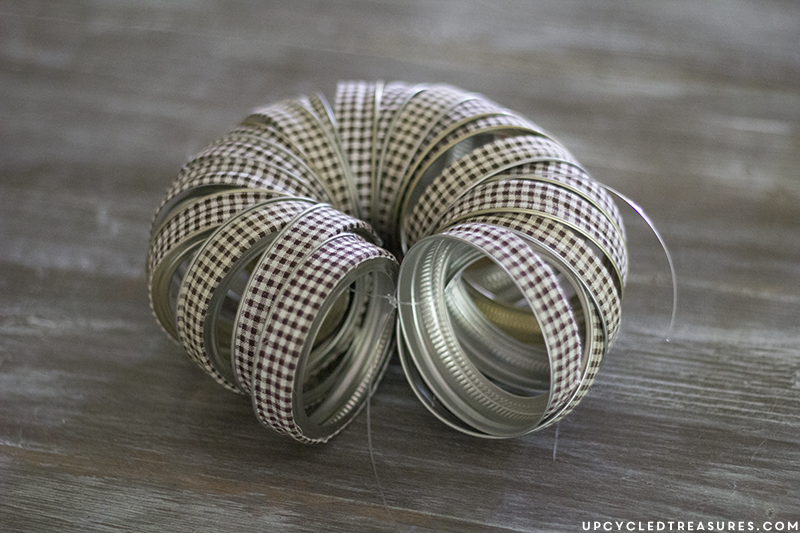 See how easy it is to create this rustic fall mason Jar lid pumpkin using canning lids, fabric tape, fishing line and a stick!