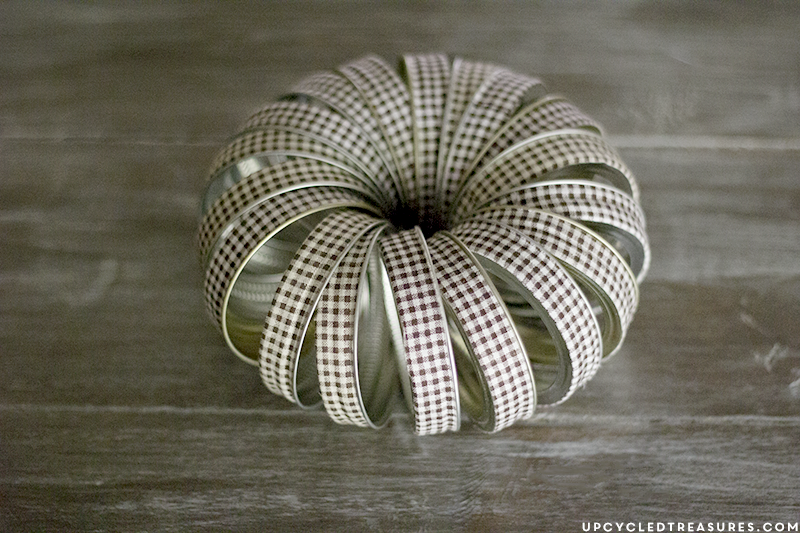 See how easy it is to create this rustic fall mason Jar lid pumpkin using canning lids, fabric tape, fishing line and a stick!