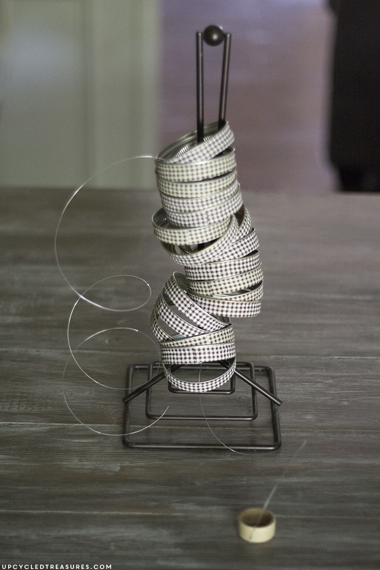 See how easy it is to create this rustic fall mason Jar lid pumpkin using canning lids, fabric tape, fishing line and a stick!