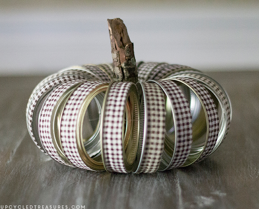 See how easy it is to create this rustic fall mason Jar lid pumpkin using canning lids, fabric tape, fishing line and a stick!